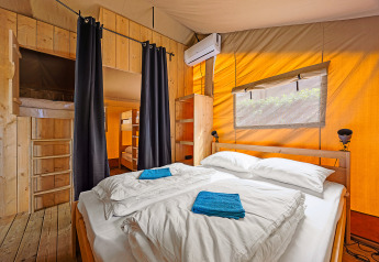 Vista interna di una tenda safari con letto matrimoniale, letti a castello, aria condizionata e arredo in legno in Croazia.