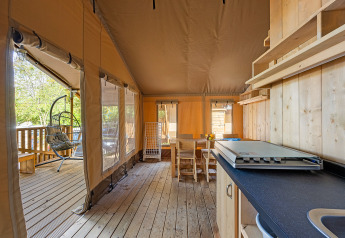 Intérieur d'une tente safari avec plancher en bois, coin repas, cuisine et fauteuil suspendu en Croatie.
