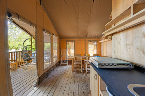 Vista interior de una tienda safari con suelo de madera, comedor y silla colgante en Camping Bijela Uvala.