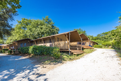 Tienda safari con baño y aire acondicionado en Camping Bijela Uvala, Croacia, rodeada de vegetación.