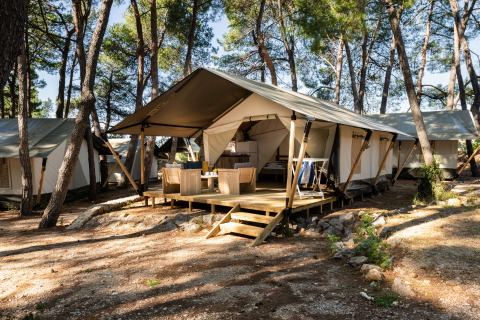Safari Tent Comfort nei boschi con veranda, mobili da esterno e diverse tende tra gli alberi.