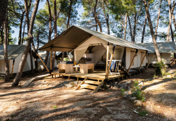 Safari Tent Comfort in het bos met veranda, buitenmeubilair en meerdere tenten tussen de bomen.