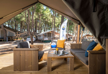 Zona de estar exterior en una tienda Safari Tent Comfort en Camping Krk, Croacia, rodeada de pinos.