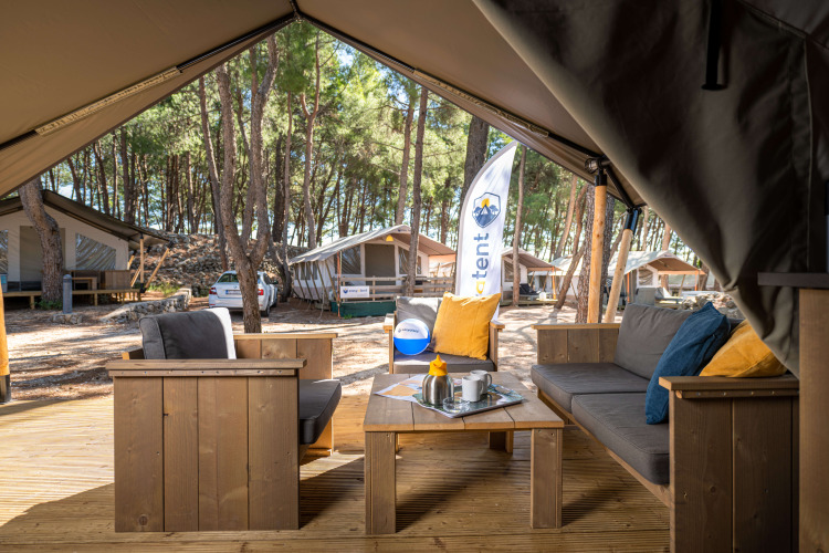 Coin salon extérieur de la Safari Tent Comfort au Camping Krk en Croatie, avec meubles en bois et pins.