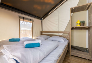 Indvendig udsigt over Safari Tent Comfort på Camping Krk i Kroatien med seng, håndklæder og hylde.