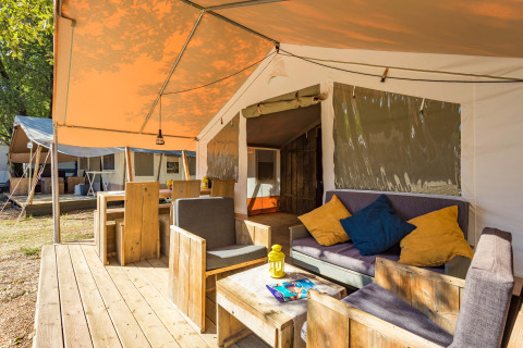 Safari Tent Luxury con terraza de madera, cómodos asientos y cojines coloridos en camping natural.