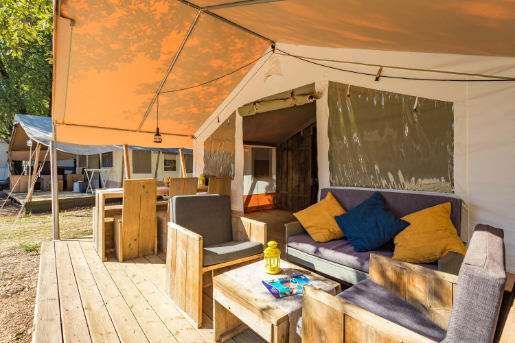 Safari Tent Luxury con terraza de madera, cómodos asientos y cojines coloridos en camping natural.