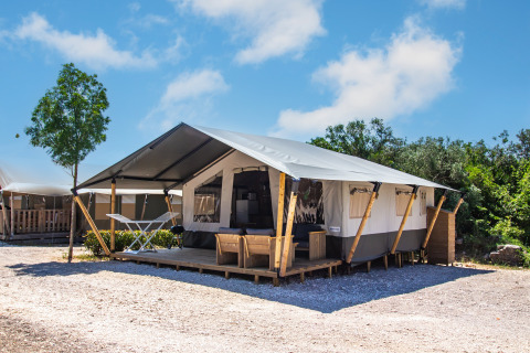 Tienda safari con baño privado y aire acondicionado, ubicada en un camping con terraza y muebles de exterior.