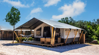 Safaritent met eigen sanitair en airconditioning op een camping, voorzien van veranda en tuinmeubilair.
