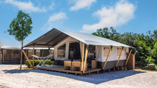 Tenda safari con bagno privato e aria condizionata, situata in campeggio con veranda e mobili da esterno.