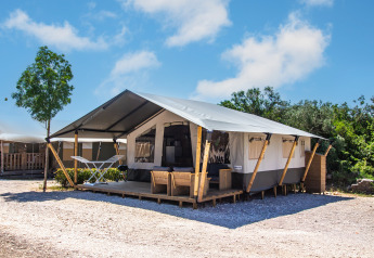 Tenda safari con bagno privato e aria condizionata, situata in campeggio con veranda e mobili da esterno.