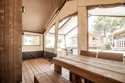 Tienda safari con mesa de madera, bancos y zona exterior en Camping Polari, Croacia, a la luz del día.