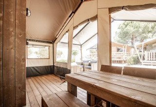 Tienda safari con mesa de madera, bancos y zona exterior en Camping Polari, Croacia, a la luz del día.