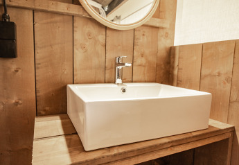 Salle de bain en bois avec lavabo carré et miroir rond dans tente safari climatisée au Camping Polari, Croatie.