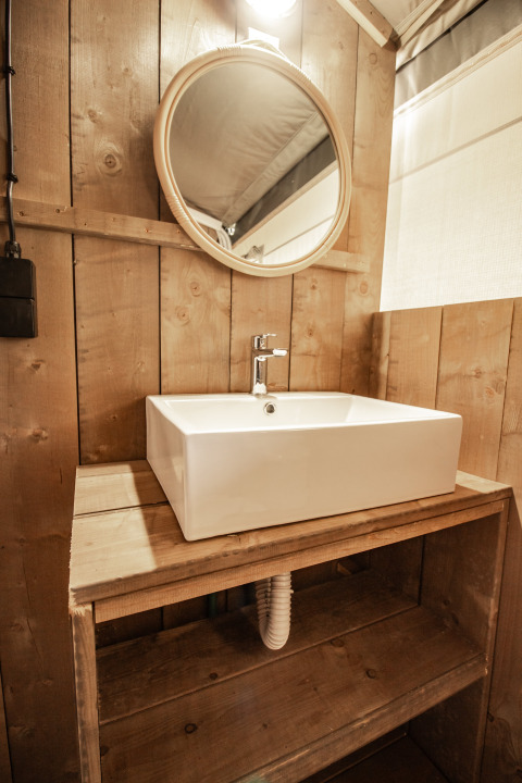 Bagno rustico con lavandino moderno e specchio tondo in tenda safari con aria condizionata a Camping Polari.