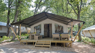 Vista exterior de una tienda safari con instalaciones sanitarias, terraza de madera y zona de estar en el bosque.