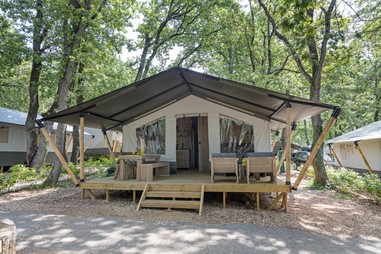 Vue extérieure d’une tente safari avec installations sanitaires, terrasse en bois et coin salon en forêt.