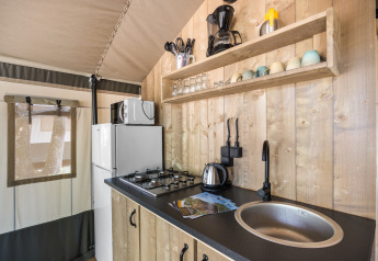 Zona de cocina en tienda safari con paneles de madera, cocina de gas, fregadero y nevera en Camping Aminess Maravea.
