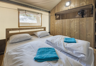 Interior de una tienda safari con cama doble, paredes de madera y ventana en Camping Aminess Maravea, Croacia.