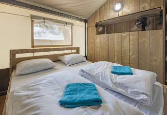 Interior de una tienda safari con cama doble, paredes de madera y ventana en Camping Aminess Maravea, Croacia.