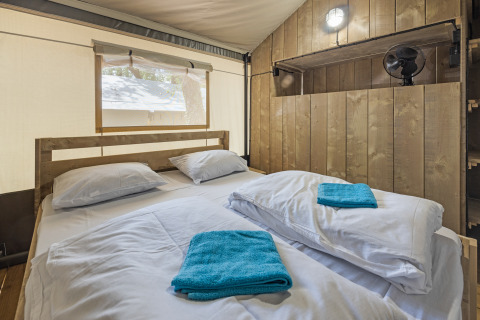 Interieur van een safaritent met tweepersoonsbed, houten wanden en raam bij Camping Aminess Maravea, Kroatië.