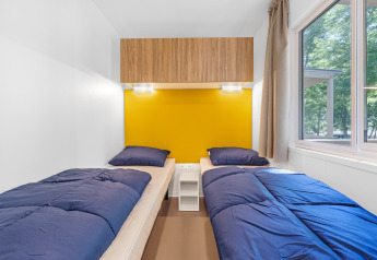 Cabina moderna con due letti singoli, biancheria blu e parete gialla nel Mobile home Porec, Camping Bijela Uvala, Croazia.