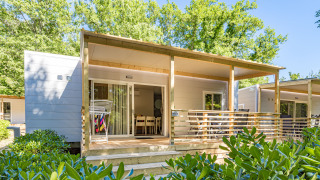 Mobilheim Porec mit überdachter Terrasse, Gartenmöbeln und Wäscheständer, umgeben von Büschen und Bäumen.