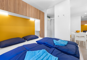 Moderne stacaravan slaapkamer met blauw beddengoed en gele wand op Camping Bijela Uvala, Porec, Kroatië.
