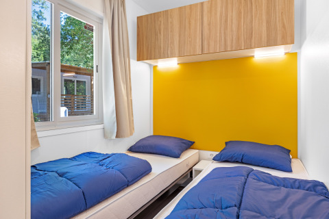 Slaapkamer in Mobile home Porec met twee single bedden, blauw dekbed en gele muur op Camping Bijela Uvala.