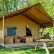 En safaritelts Forest Lodge ved Sandberghe i Nederlandene, med veranda, bænk og picnicbord i grøn natur.