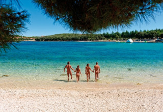 Vier Menschen laufen bei sonnigem Wetter am Koversada Camping Resort in Istrien, Kroatien, ins klare Wasser.