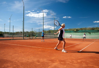 Mensen spelen tennis op een gravelbaan bij Koversada Camping Resort in Istrië, Kroatië, onder een blauwe lucht.