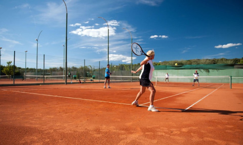 Mensen spelen tennis op een gravelveld in het Koversada Camping Resort in Istrië, Kroatië, onder blauwe lucht.