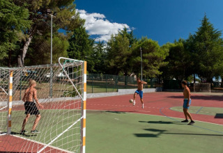 Jugendliche spielen Fußball auf einem Außenplatz im Koversada Camping Resort, umgeben von Bäumen.