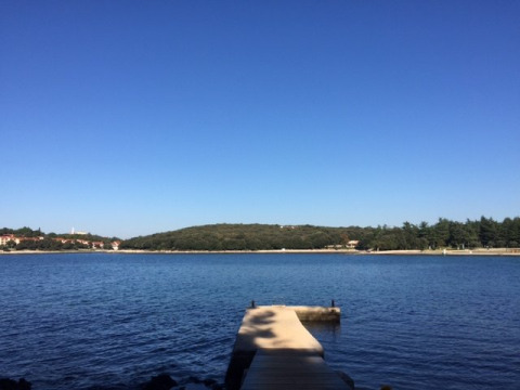 Badebro ved rolig sø med udsigt over Koversada Camping Resort i Istrien, Kroatien, under klar blå himmel.