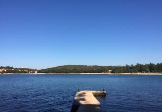 Badebro ved rolig sø med udsigt over Koversada Camping Resort i Istrien, Kroatien, under klar blå himmel.