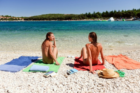 Dos personas tomando el sol desnudas en la playa de guijarros del Koversada Camping Resort, Istria, Croacia.