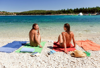 Two people sunbathing nude on a pebble beach at Koversada Camping Resort, Istria, Croatia, near the sea.