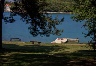 Uitzicht op zee en een zwempier bij Koversada Camping Resort in Istrië, Kroatië, met banken en bomen.