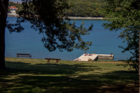 Blick auf das Meer und einen Badesteg im Koversada Camping Resort in Istrien, Kroatien, mit Bänken.