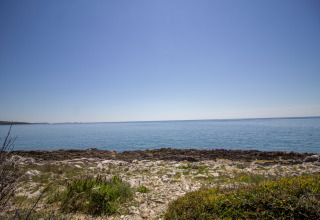 Kustzicht bij Koversada Camping Resort in Istrië, Kroatië, met rotsachtige oever, helder water en blauwe lucht.