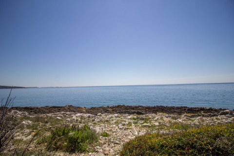 Kustzicht aan Koversada Camping Resort in Istrië, Kroatië, met rotsen, rustig water en een blauwe hemel.