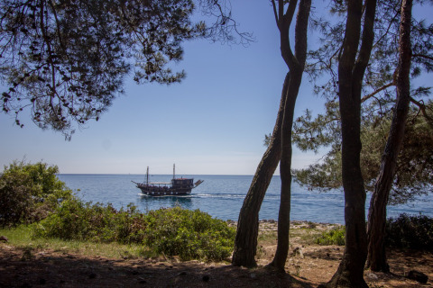 Blick vom Koversada Camping Resort in Istrien, Kroatien, auf ein Schiff auf dem Meer zwischen Bäumen.