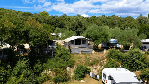 Camping Porto Sole en Istria, Croacia, con cabañas, caravana y vegetación frondosa bajo un cielo azul brillante.