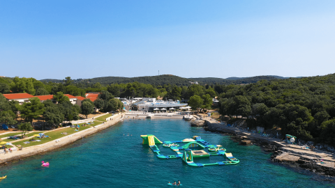 Vista aérea de Camping Porto Sole en Istria, Croacia, con playa, parque acuático hinchable y bosque.