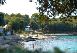 Strand med klart blåt vand og grønne træer ved Camping Porto Sole feriepark i Istrien, Kroatien.