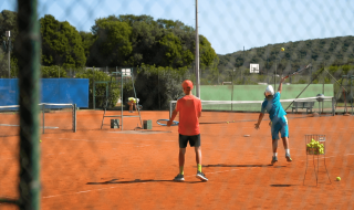 Twee kinderen spelen tennis op een rood gravelveld in Camping Porto Sole, een vakantiepark in Istrië.
