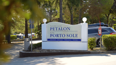 Cartello d’ingresso del Camping Porto Sole e del villaggio turistico Petalon a Istria, Croazia, tra alberi e auto.