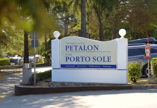 Cartello d’ingresso del Camping Porto Sole e del villaggio turistico Petalon a Istria, Croazia, tra alberi e auto.