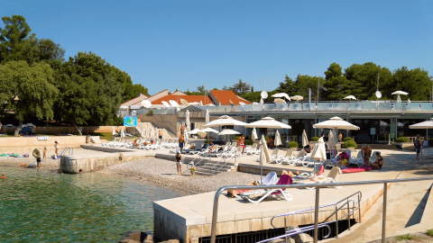 Lettini e ombrelloni al sole sulla spiaggia del Camping Porto Sole in Istria, Croazia, con persone che si rilassano.